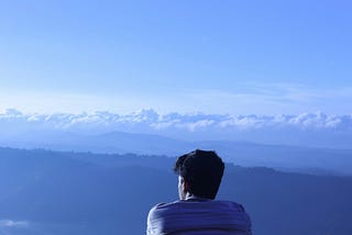 Man sitting with back facing photo looking over a mountain ledge.