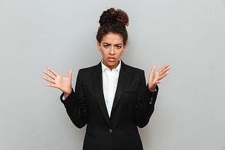 Confused Black woman in a business suit standing against a gray wall