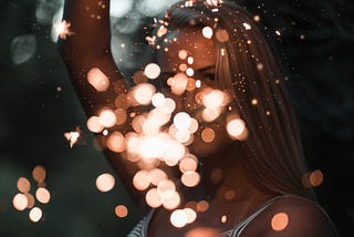 A woman holding a sparkler with a spray of lighted dots in front of her face.