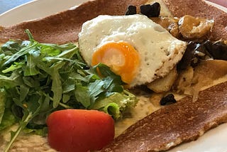 A crepe with an egg, ruccula salad and a piece of a tomato.