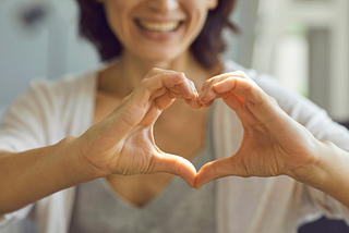 Woman smiling extending her hands in the shape of a heart