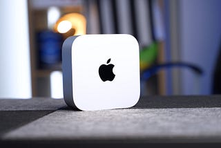 M4 Mac mini stood up on a light and dark grey fabric desk.