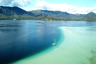 A sailboat anchored in a bay of green and blue waters.