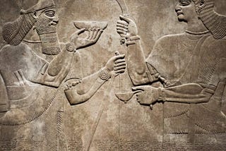 Stone relief of 2 Sumerian Gods facing each other and holding a cup and tools