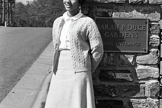 Wilhelmina Reuben, May Queen 1967, leans on a stone column with a plaque that says, “Sarah P. Duke Gardens, Main Entrance.”