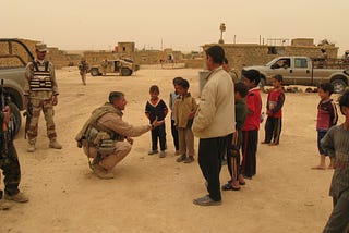 Man in military uniform shakes hands with Iraq children