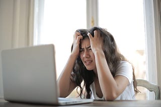Young woman in white T-Shirt sitting at her laptop showing frustration