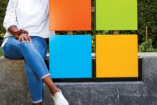 A young woman sits next to the iconic Microsoft logo and symbol.