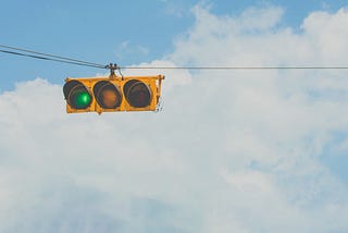 A set of traffic lights on a wire, with the green light illuminated