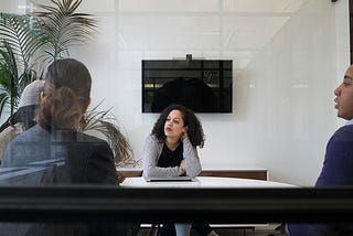 Photo of a professional woman in a work meeting, surrounded by colleagues