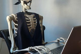 Plastic skeleton sitting by a computer and a shot glass