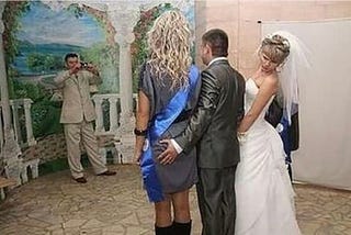 The bride standing on the right looking where her husbands left hand is at a photo shoot.