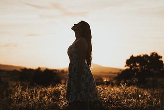 A woman standing in a field at dawn.