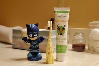 A giraffe-themed child’s toothbrush, children’s toothpaste, and a PJ Masks bath toy.