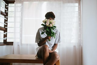 A black woman with a bouquet of flowers hiding her face.