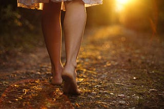 Young girl legs walking barefoot through a forest toward the sunset. It represents the innocence of a young girl stepping into the dangerous vicious cycle of dieting and emotional eating for the first time.