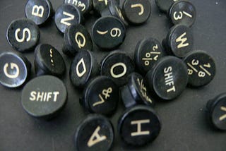 about 25 round keys from a typewriter (with letters, numbers, and punctuation on them) that have been removed from the typewriter and are lying randomly on a black surface