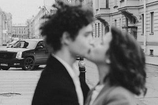 Black and white and lightly off-focus photograph of a couple kissing on the street.