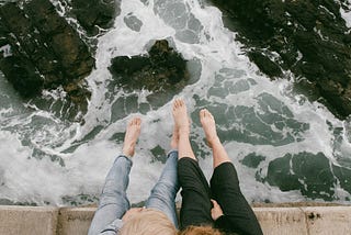 A man and woman sit, embracing, above choppy water.