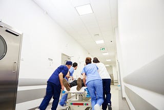 Hospital staff rush a patient down a hospital hallway on a gurney.