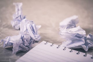 A notepad next to discarded balled up pieces of paper