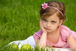 bored princess girl in pink headband resting chin in hand