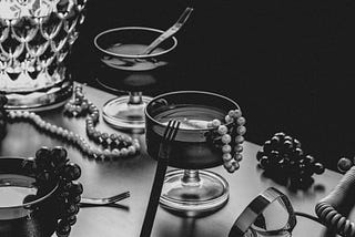 A vanity table holding cocktails, a pearl necklace and a vintage lamp.