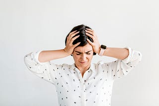 A stressed woman with dark hair holds her head in between her hands in a sign of frustration.