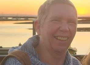 photo of author, wearing a sweater, with short hair spiked up, smiling, by a sunset background