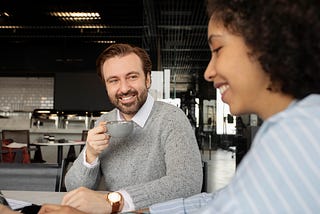 A close-up photograph of two people sitting across in a coffee shop.