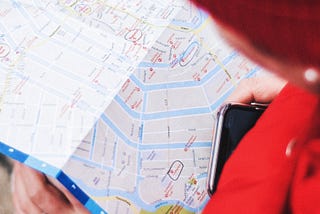 Woman with smartphone glancing at a paper map.