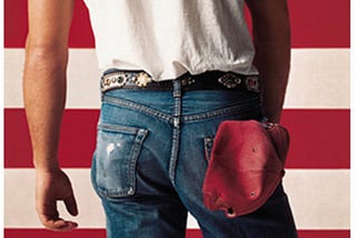 Bruce Springsteen’s Born in the U.S.A. album cover of his backside, wearing blue jeans with a red hat in the back pocket and a white t-shirt, facing the red and white stripes of a flag.