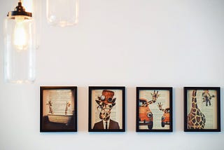 Four framed photos of illustrated giraffes on a white wall