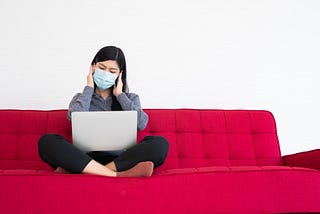 A woman working on her laptop with hands on head.