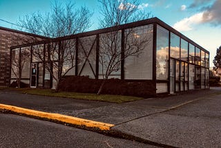 a modernist glass and steel one-story building with a blue evening sky reflecting off of its side windows