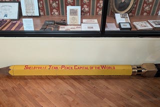 Oversized model of a pencil lying on the floor in front of a museum display case.