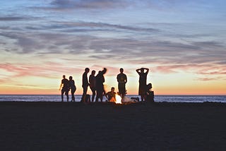 Group of friends around a bonfire at dusk.