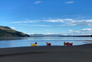 A yellow and two red canoes empty on the banks of the Yukon river.