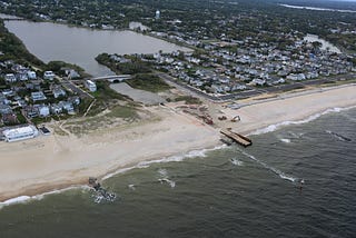 Aerial photo of coastal community. Beach separates the ocean from a waterway leading to a pond. Heavy machinery is working on the beach