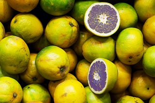 A group of oranges are piled on top of each other and one is cut open. It’s a sickly shade of purple.