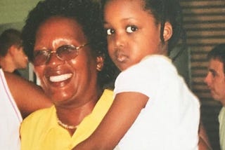 photograph of a black toddler looking warily at the camera, in the arms of an older black woman, who is smiling widely; the writer and her grandmother.