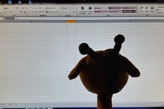 Image shows the head and part of the neck of a plush giraffe silhouetted against an empty spreadsheet displayed on a computer monitor.