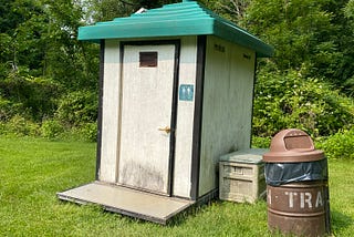 Photo of a porta potty with a trash can next to it