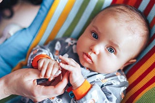 baby holding parent’s hand while looking at camera