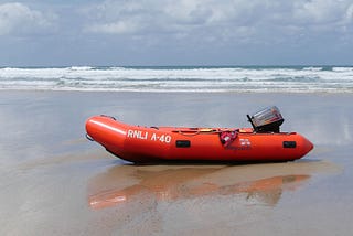 An orange lifeboat sitting in a cloudy beach.