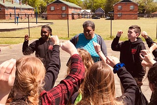 Students standing in circle with adult woman with fists in the air