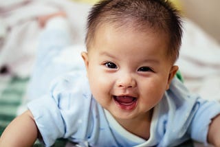 Baby boy lying on stomach with arms propped up, winking.