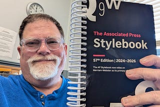 The author, John Carney, holding a spiral-bound 2024–26 Associated Press Stylebook.