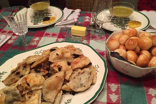 Plates with pierogi, bobalki, and glasses of pea soup sitting on top of a red, white, and green Christmas table cloth.