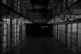 Black and white photo of a prison complex: multiple cells, just bars upon bars receding into shadow.